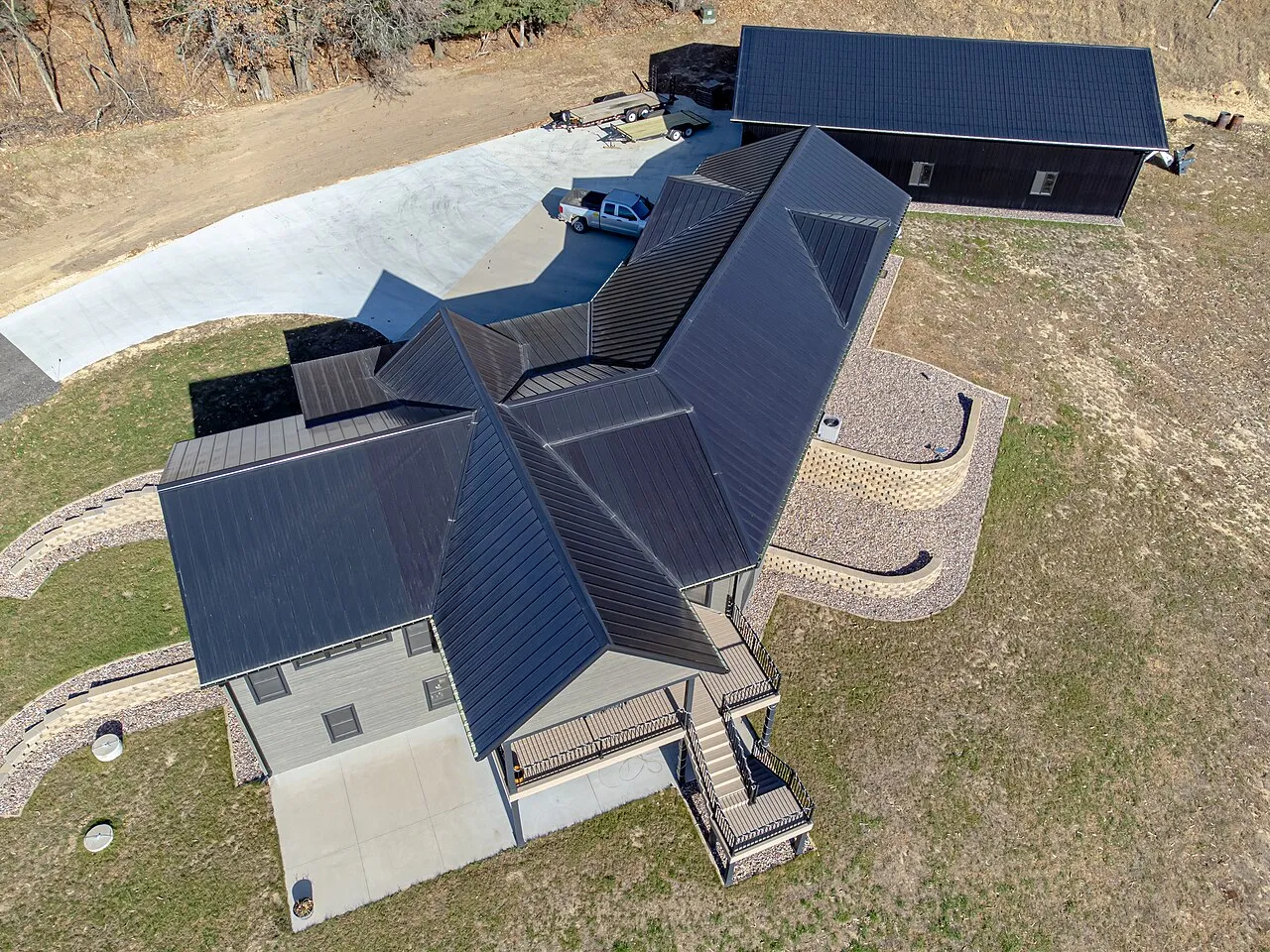 Aerial view of a rural home and garage with black standing seam metal roofs
