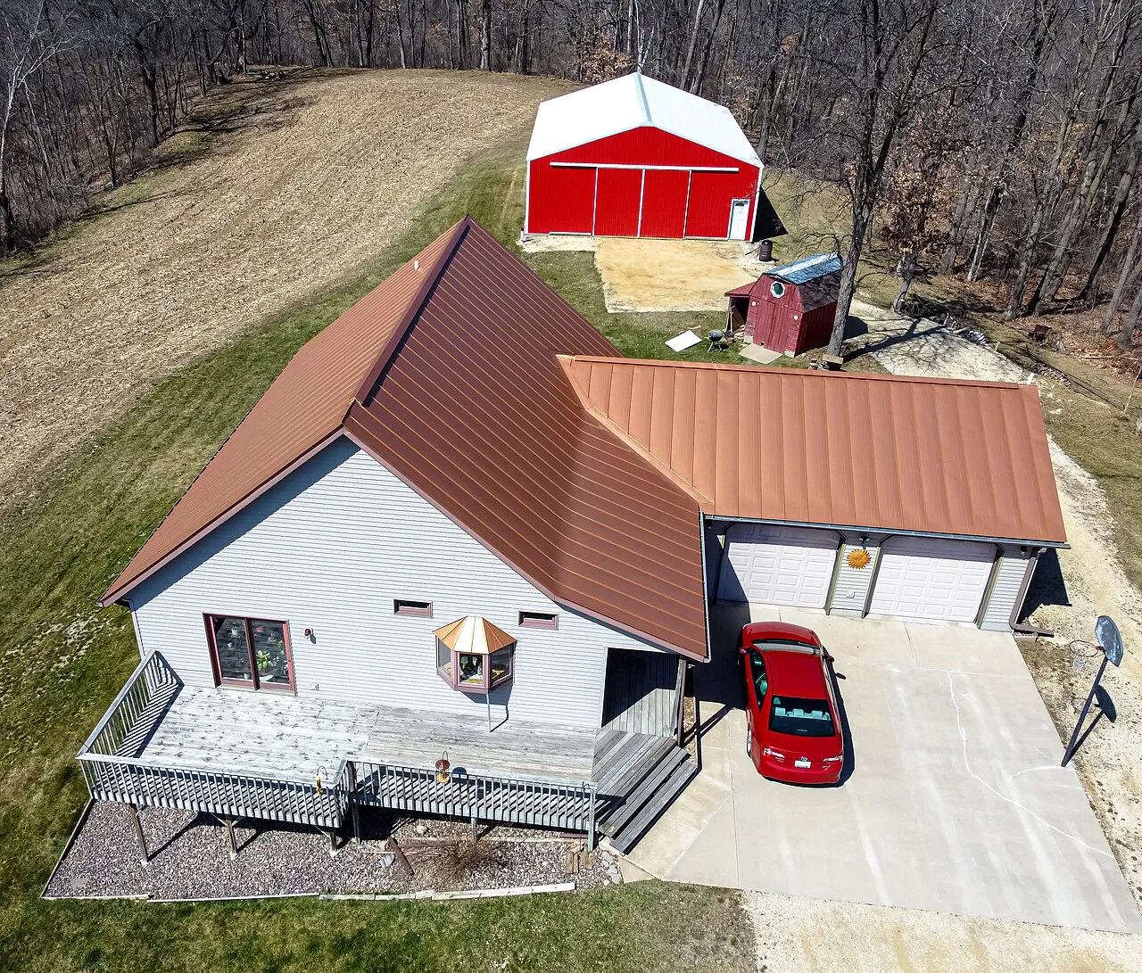 Aerial view of a white house with a copper-colored metal roof and a red barn behind it
